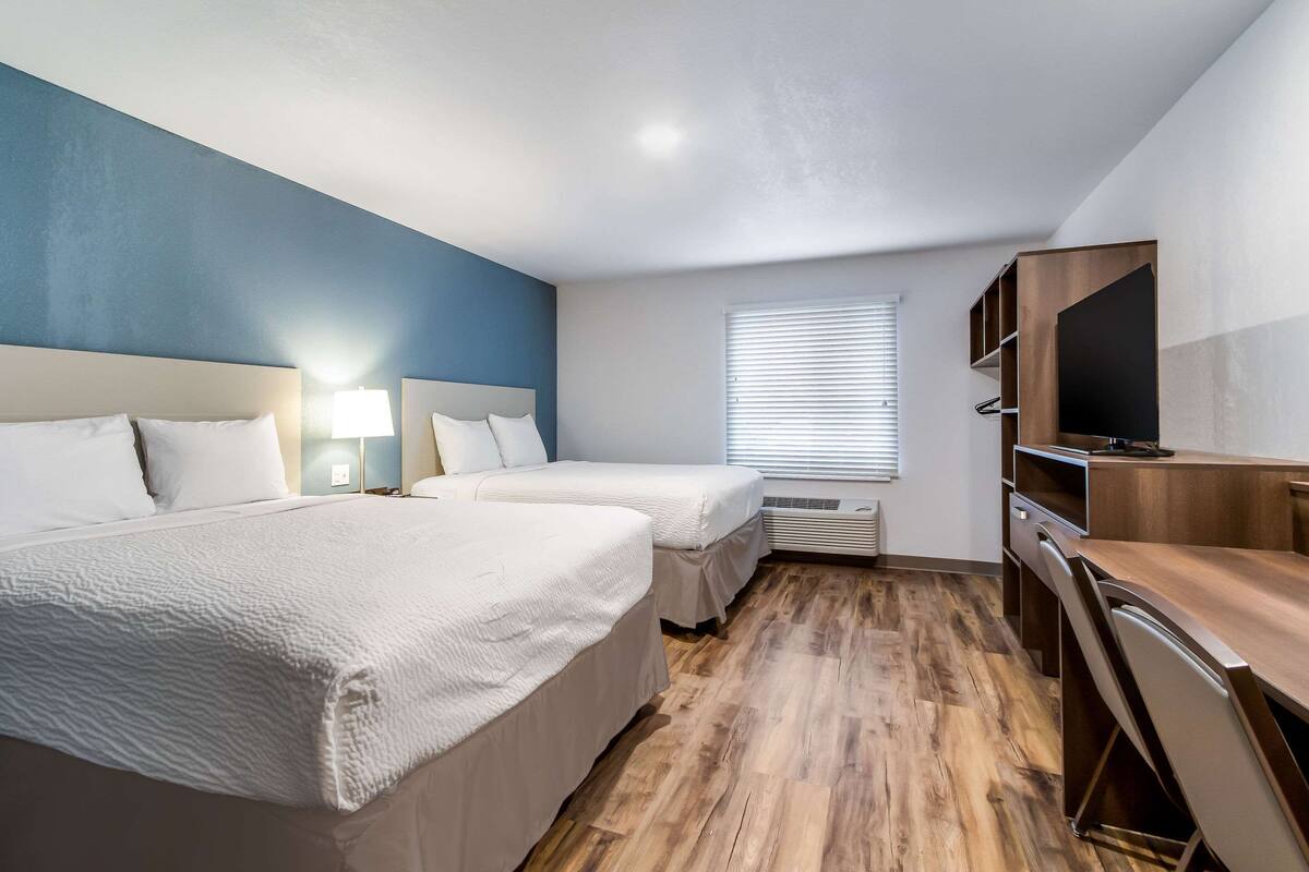 Een hotelkamer met twee bedden, een bureau, een televisie en een raam met jaloezieën.