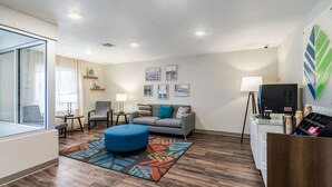 A modern living room with a sofa, ottoman, and chairs, a coffee station, and framed pictures on the wall. - WoodSpring Suites Harrisburg Linglestown (Harrisburg)
