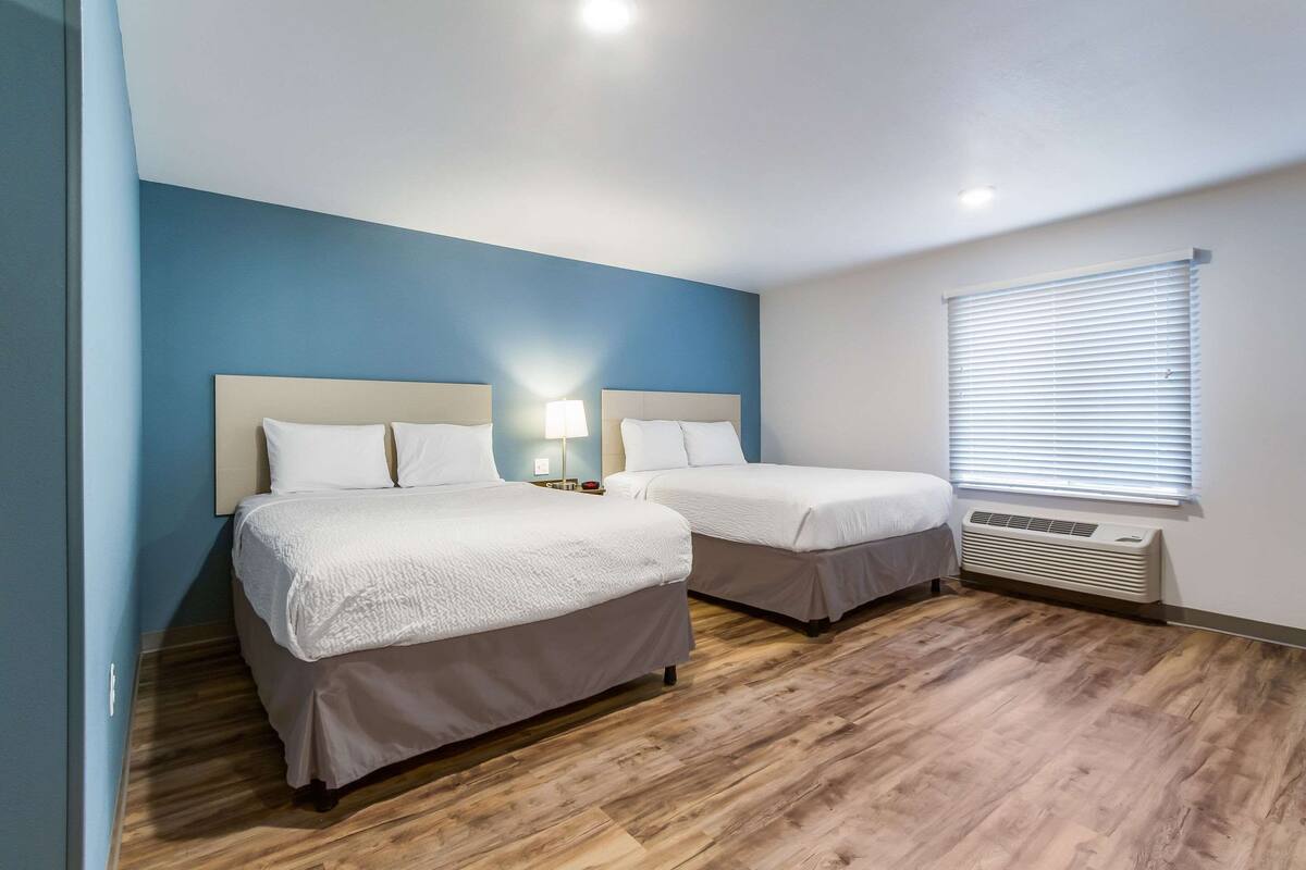 Een hotelkamer met twee bedden, een raam met zonwering, een verwarming en een nachtkastje met een lamp.