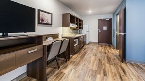 A modern kitchen with wooden cabinets, a built-in microwave, and a dining area with a table and chairs. - WoodSpring Suites Harrisburg Linglestown (Harrisburg)