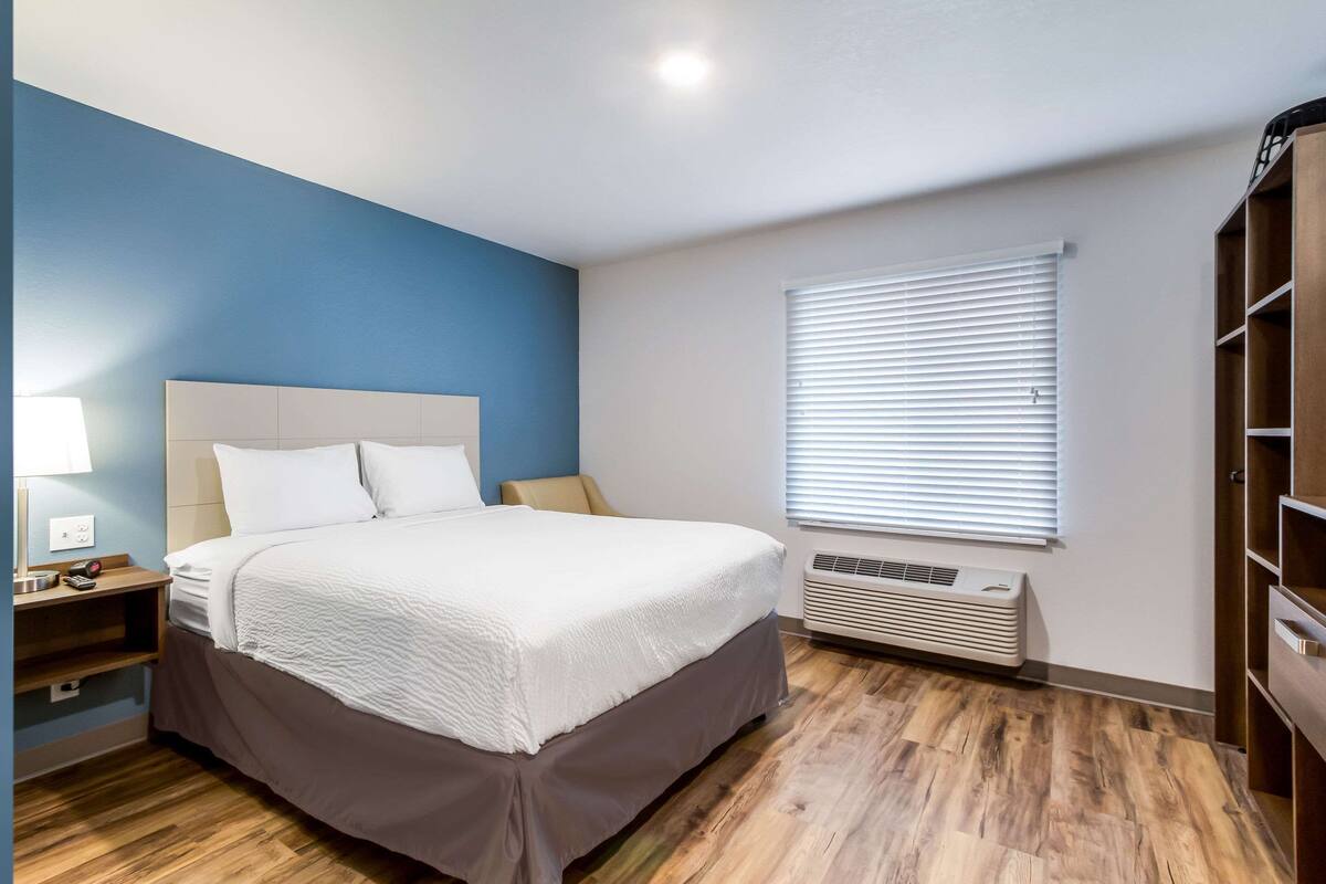 Een slaapkamer met een bed, nachtkastje, lamp en een raam met jaloezieën.