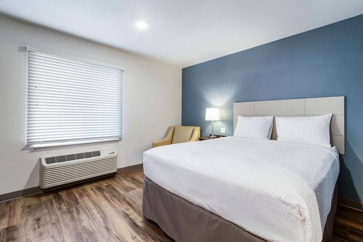 Een hotelkamer met een groot bed, een stoel, een lamp en een raam met jaloezieën.