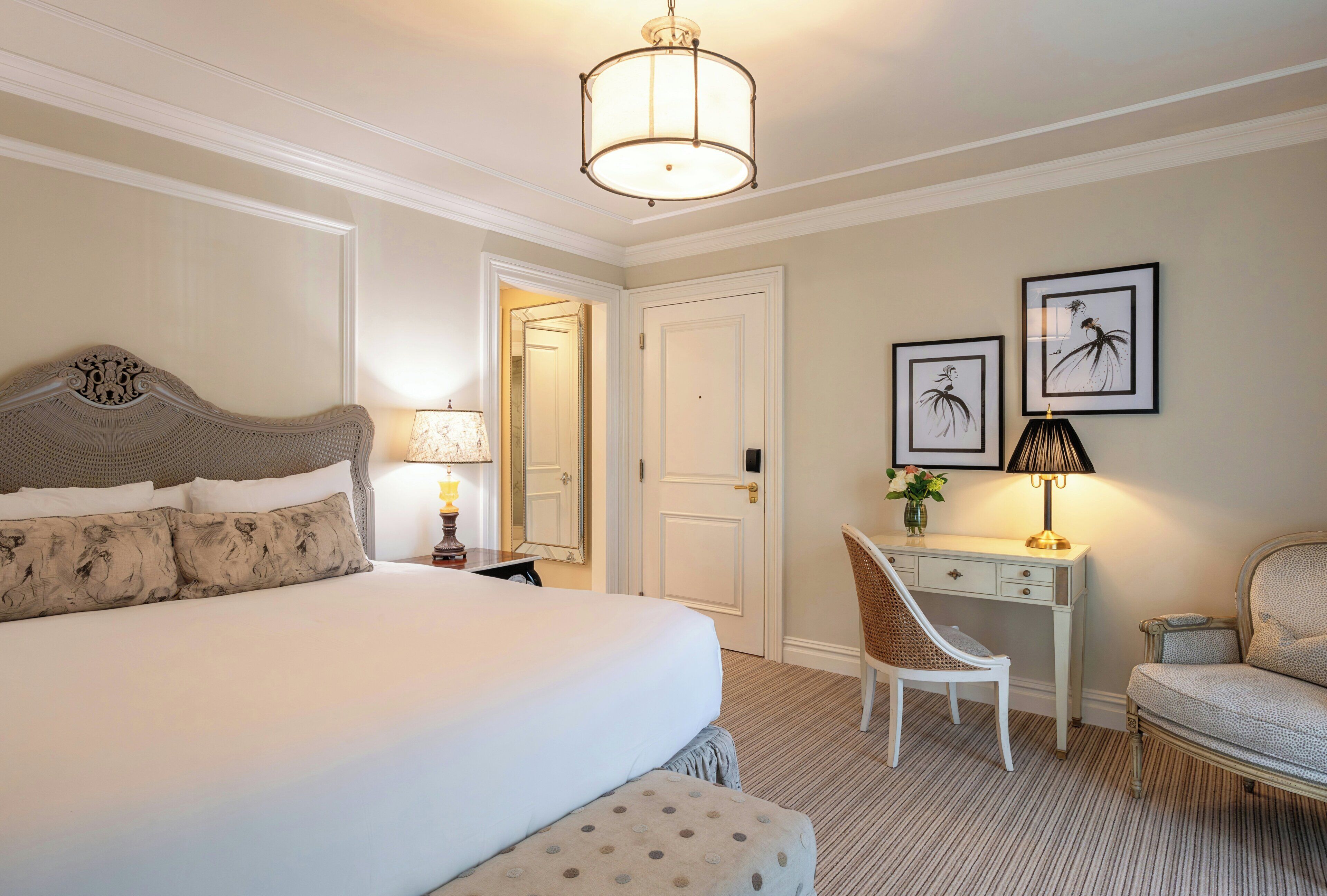 A hotel room with a large bed, a desk, a chair, and artwork on the wall.