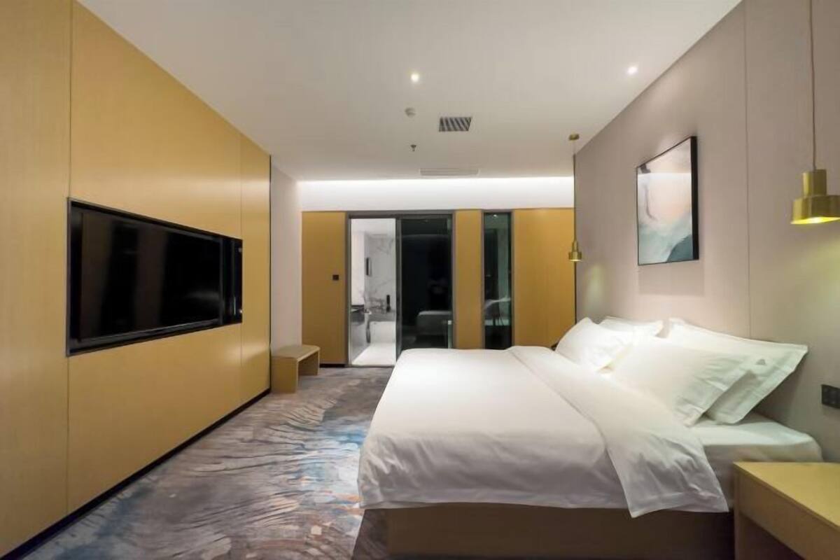 Ett modernt hotellrum med en stor säng, en platt-TV som är monterad på väggen och en dörr som leder till badrummet.