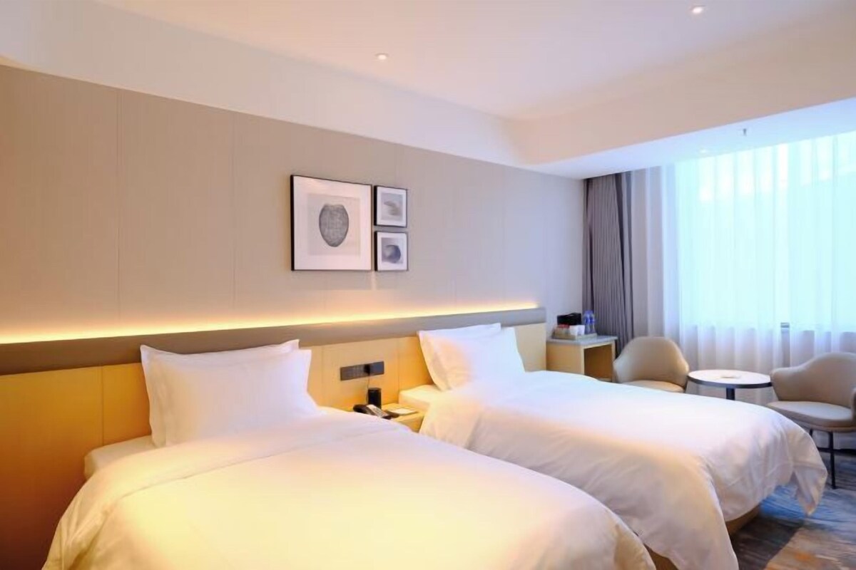 A hotel room with two beds, a bedside table, a chair, and a small round table.