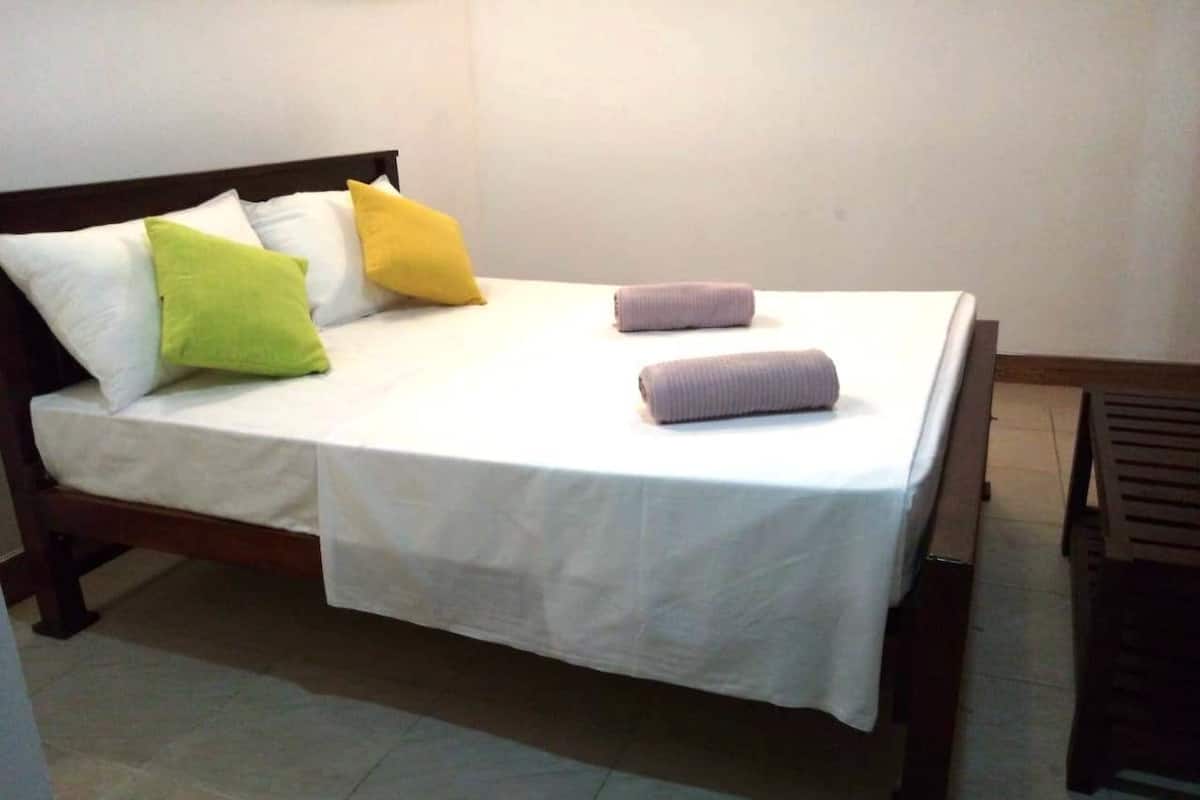 Una cama bien hecha con sábanas blancas, una almohada verde y dos toallas enrolladas.