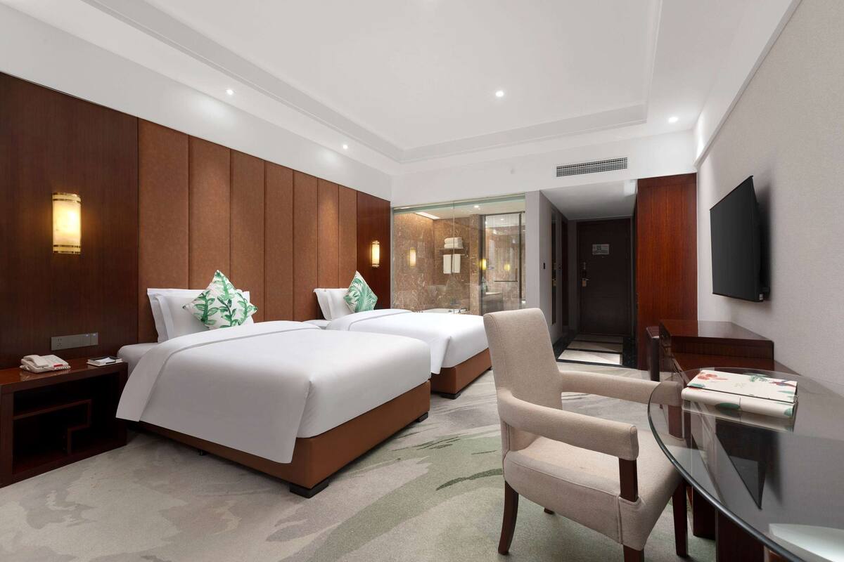 A hotel room with two beds, a TV, a glass table, and a chair.