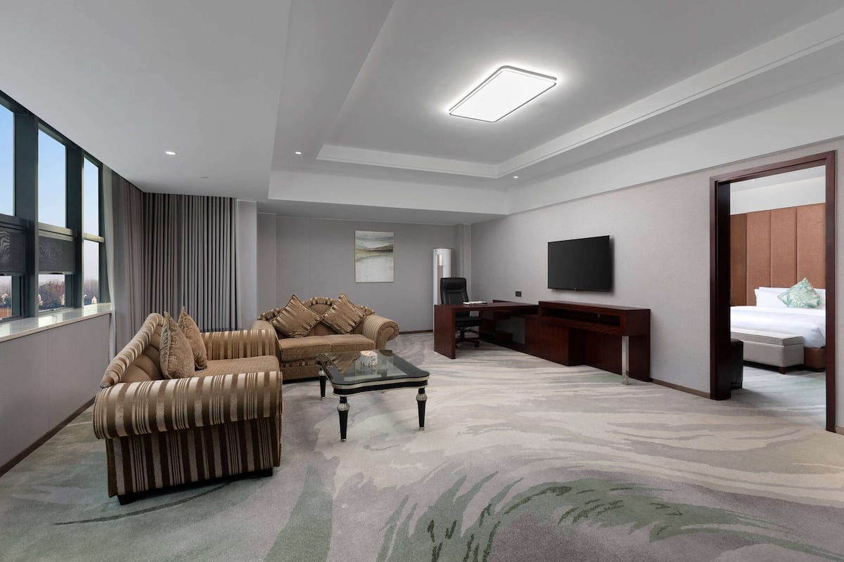A modern hotel room with a sofa, a coffee table, a desk, a flat-screen TV, and a bed.