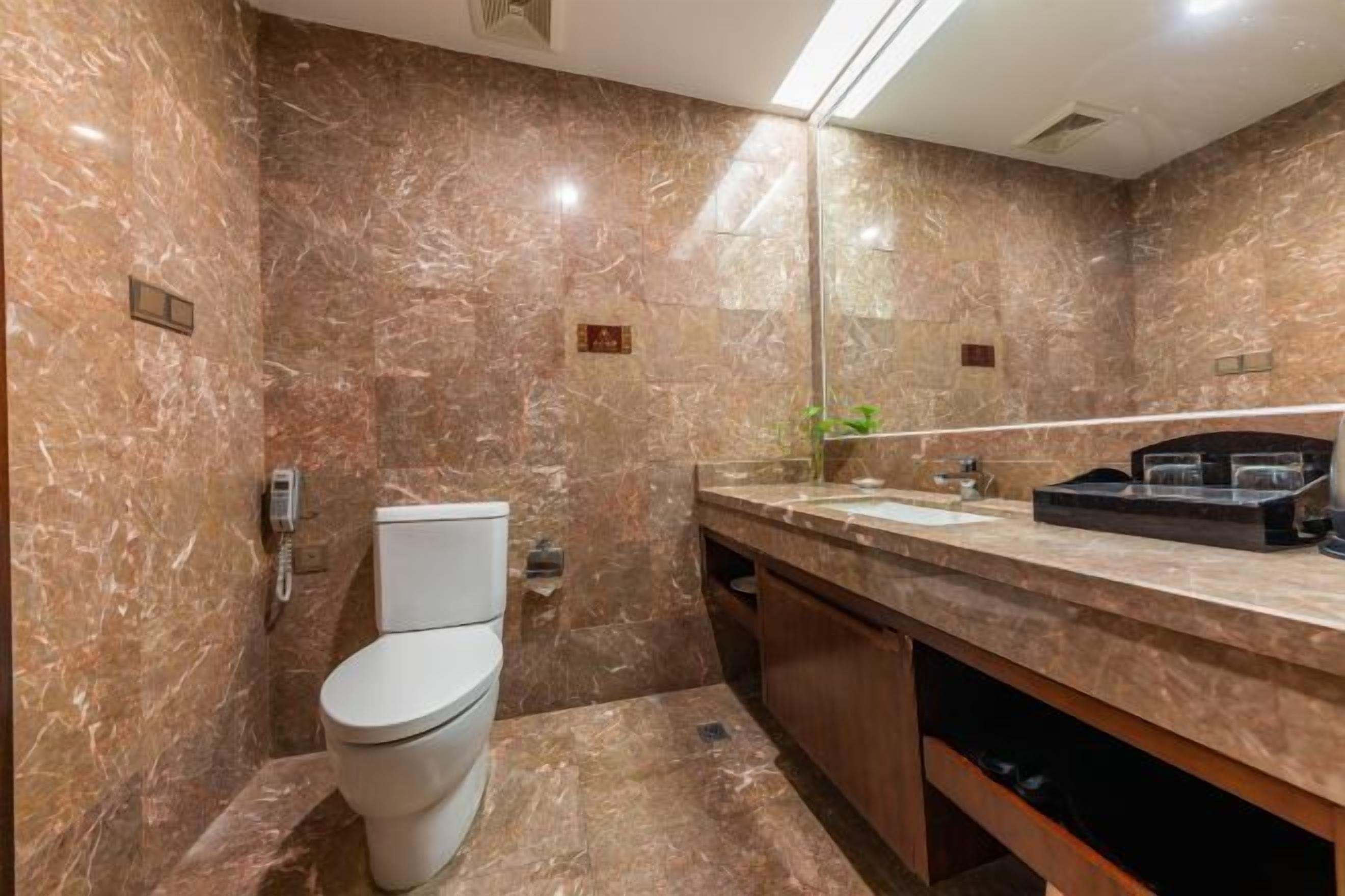 A modern bathroom with a marble wall, a toilet, a sink, and a mirror.