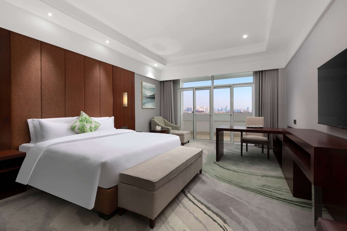 A hotel room with a large bed, a desk, a chair, and a television.