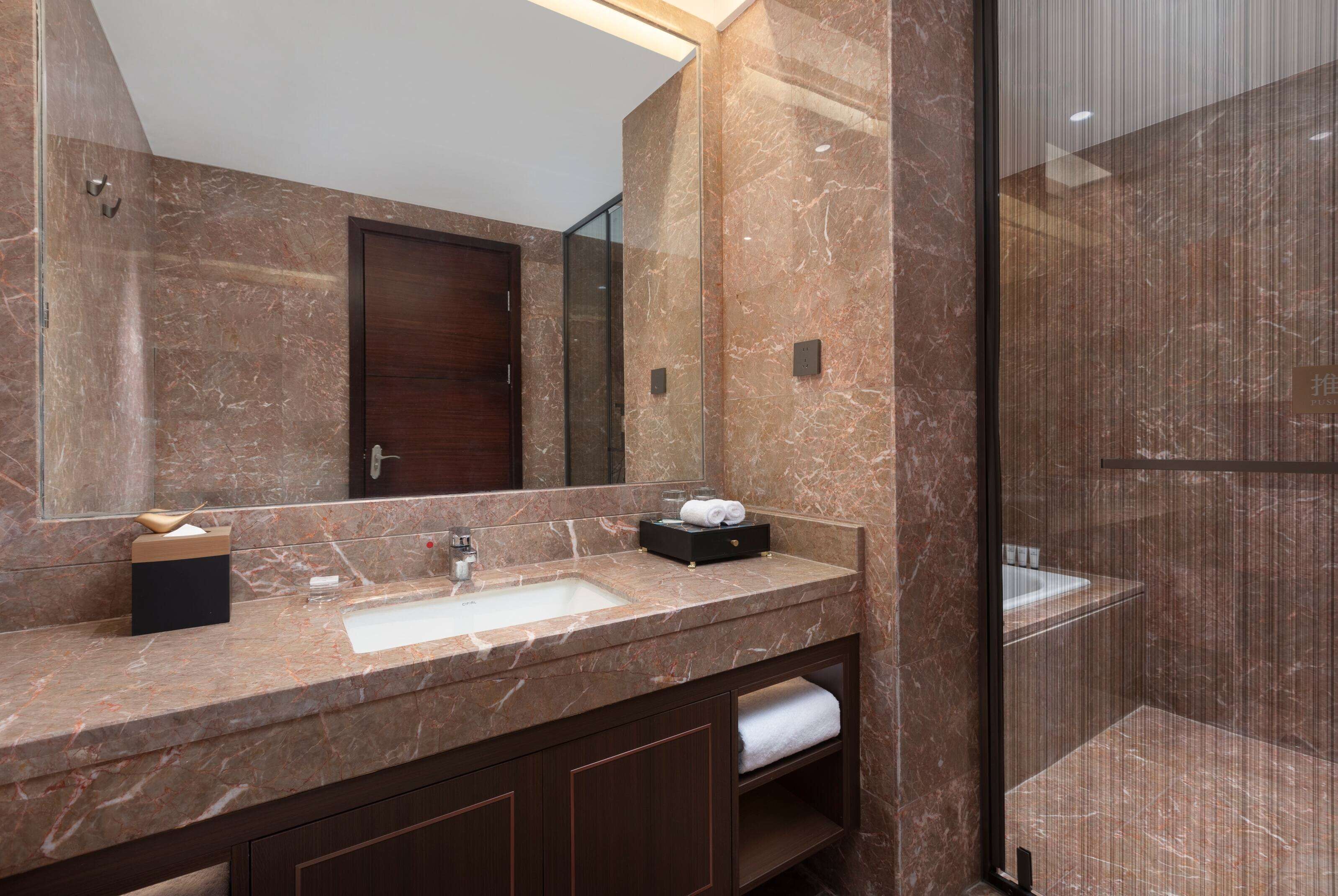 A bathroom with a marble sink, dark wood cabinets, a large mirror, and a glass shower enclosure.