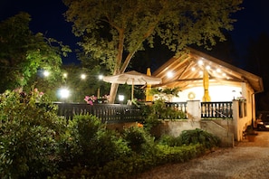 A nighttime outdoor seating area with string lights, a covered patio, and lush greenery.