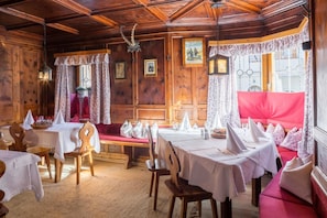 A traditional inn with wooden walls and ceilings, a dining area with tables set for two, and a cozy seating area with a red sofa.