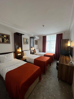 A hotel room with three beds, a desk, a TV, and artwork on the walls. - Topkapi Hotel (Istanbul)