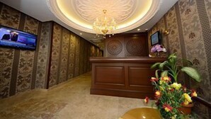 Zona de recepción de un hotel con un mostrador de madera, un televisor en la pared y una araña.
