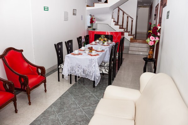 A dining area with a table set for four, surrounded by chairs, a red sofa, and a white couch.