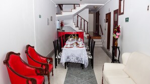 Ein Essbereich mit einem Tisch für vier Personen, roten Polstersesseln, einem weißen Sofa und einer Treppe im Hintergrund.