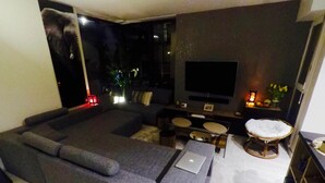 A modern living room with a grey sectional sofa, a flat-screen TV, a small coffee table, and a wicker chair. - Charming and cosy rooms (Reze)