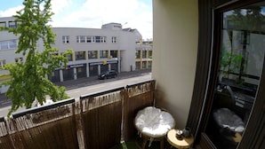 A balcony with a view of a street, a wicker fence, a small round table, and a cushioned chair. - Charming and cosy rooms (Reze)