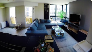 A modern living room with a sectional sofa, a flat-screen TV, and a large window offering a view of the outside. - Charming and cosy rooms (Reze)