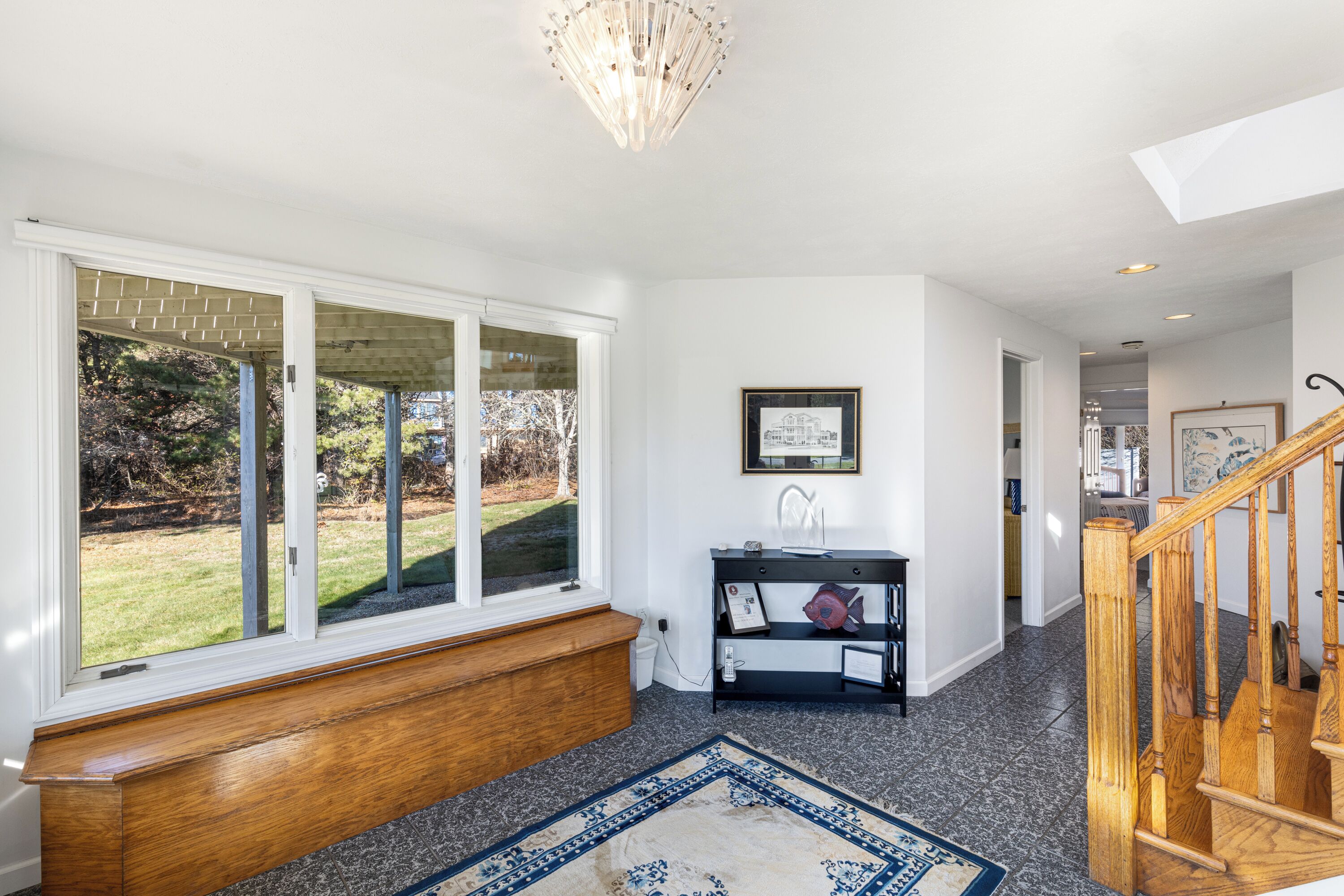 A spacious entryway with a wooden bench, a black console table with a fish decoration, and a blue patterned rug.