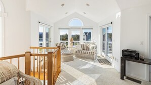 A bright, spacious room with a high ceiling, large windows, wicker furniture, and a printer on a table.