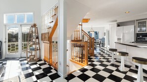 A modern kitchen with a checkered floor, wooden staircase, and a view through the glass door.