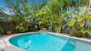 Piscina cercada por plantas tropicais exuberantes e uma cerca de madeira.
