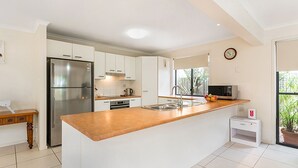 Uma cozinha moderna com armários brancos, geladeira de aço inoxidável, bancada de madeira e uma pia.