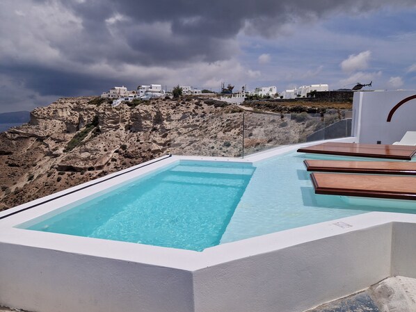 A rooftop infinity pool with clear blue water, surrounded by white walls and wooden deck chairs. - Caldera View Private Villa with Private Pool / Heated Jacuzzi / Amazing Sunset (Thira)