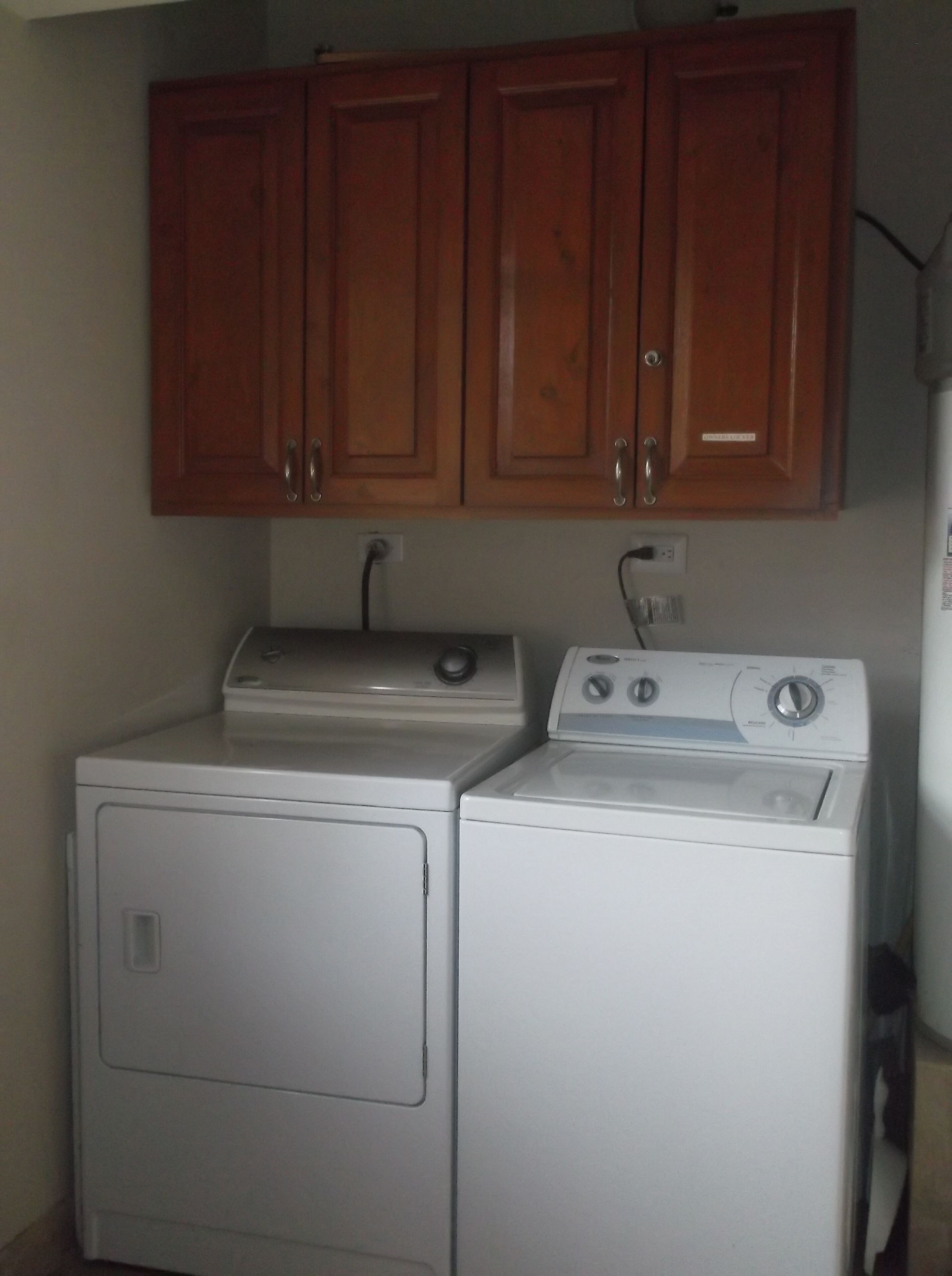 A laundry area with two white washing machines and wooden cabinets above.