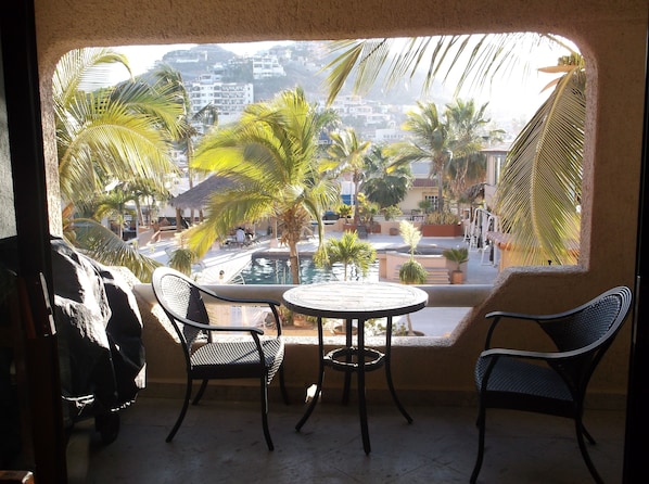 A balcony with a view of a pool, palm trees, and buildings.