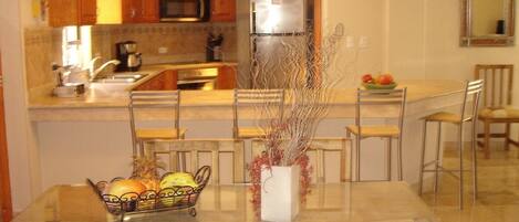 A modern kitchen with wooden cabinets, stainless steel appliances, and a dining area with a glass table and metal chairs.