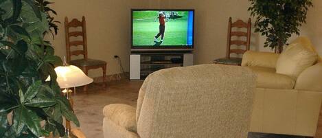 A living room with a television displaying a golf game, a beige armchair, a yellow sofa, and a large green plant.
