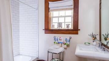 A bathroom with a white bathtub, a sink, and a mirror. There is a window with a wooden frame and a towel rack with towels.