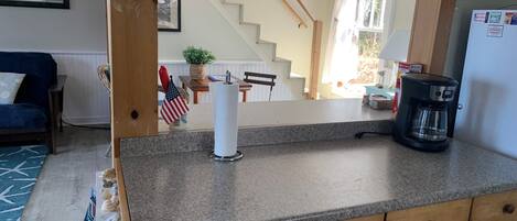 A kitchen with granite countertops, wooden cabinets, a coffee maker, and a view of a staircase leading to a dining area.