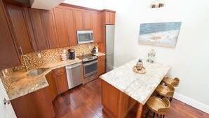 A compact kitchen with wooden cabinets, a microwave, a refrigerator, and a small dining area with stools. - 2 Bedrooms w/Loft, Deck  and  Fireplace on Thames St (Newport)