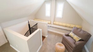 A loft bedroom with a high ceiling, a built-in bench with cushions, a brown leather armchair, and a small round ottoman. - 2 Bedrooms w/Loft, Deck  and  Fireplace on Thames St (Newport)