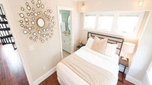 A bedroom with a large bed, a wall-mounted mirror, and a window with blinds. - 2 Bedrooms w/Loft, Deck  and  Fireplace on Thames St (Newport)