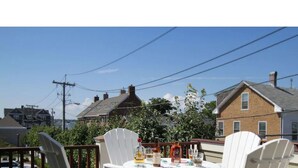 A dining area with a table set for two, surrounded by white chairs, with a view of houses and power lines in the background. - 2 Bedrooms w/Loft, Deck  and  Fireplace on Thames St (Newport)