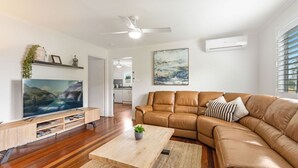 Un salon moderne avec un canapé en cuir, un téléviseur à écran plat, un plancher en bois et un ventilateur de plafond.