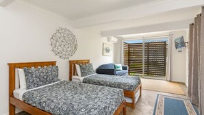 Une chambre avec deux lits, une tête de lit en bois, une literie à motifs, une chaise, un élément décoratif mural et une vue sur l’extérieur par une porte coulissante.