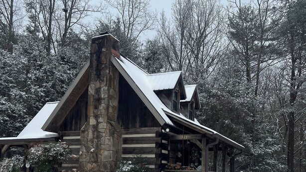 Una cabaña de troncos con chimenea de piedra, revestimiento de madera y techo cubierto de nieve.