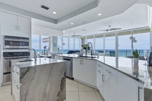 A modern kitchen with a large marble island, built-in appliances, and a view of the ocean.