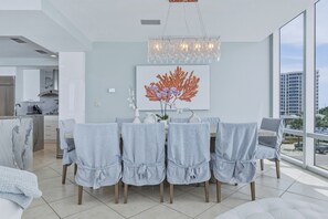 A modern dining area with a marble island, grey upholstered chairs, and a large window offering a city view.