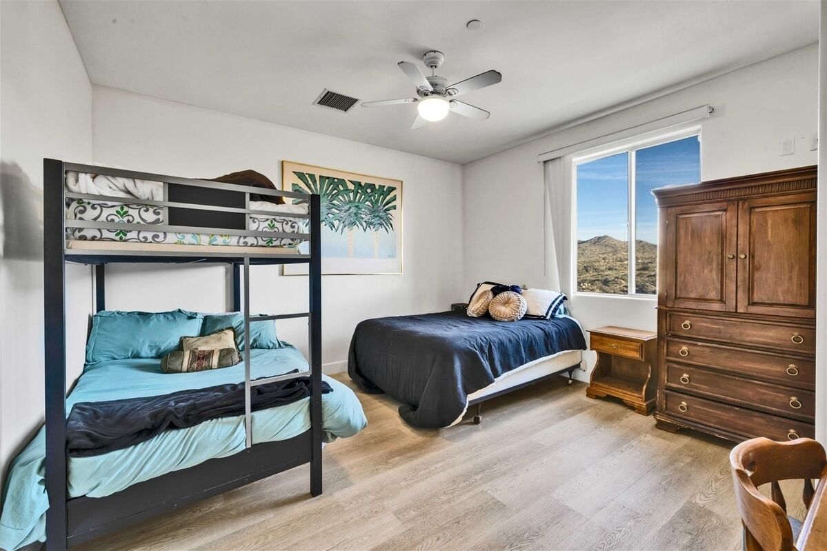 Ein Schlafzimmer mit Etagenbett, Einzelbett, Holzkommode, Deckenventilator und Fenster mit Landschaftsblick.