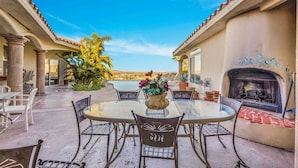 An outdoor patio with a round glass table, metal chairs, a fireplace, and a view of the desert landscape. - ** 4BR, Absolute Privacy, Jacuzzi, Pool Heating Can Be Added** (Palm Springs)