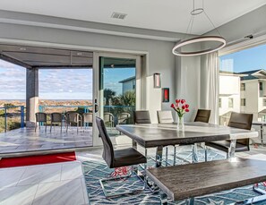 A modern dining area with a large table, chairs, and a vase of red flowers. - Private Heated Pool, Beach Access, All King Beds (Tybee Island)