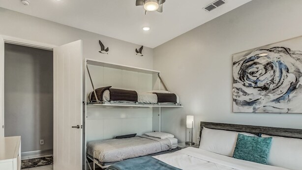 A bedroom with a bunk bed, a single bed, a large abstract painting, and a bedside table with a lamp.