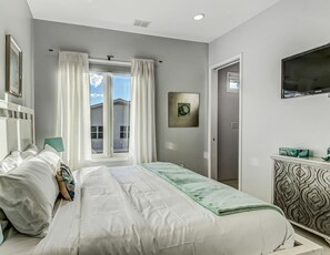 A bedroom with a bed, a nightstand, a dresser, a television, and a window with curtains. - Private Heated Pool, Beach Access, All King Beds (Tybee Island)